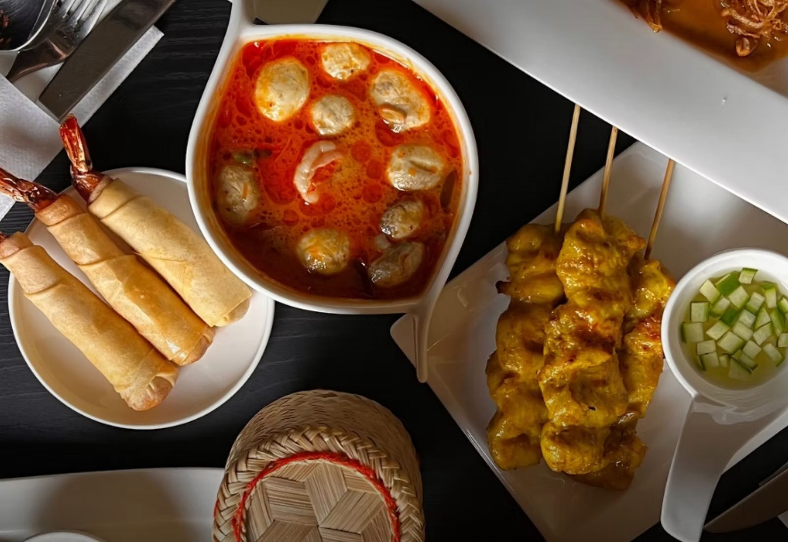 A Thai table at Tom Yam: hot and sour soup, spring rolls, chicken satay skewers and a basket of sticky rice